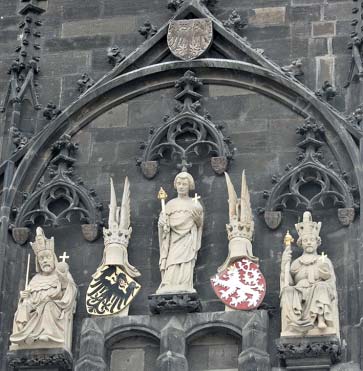 Die Wand einer Kirche oder Kathedrale ist zu sehen. Der dunkelgraue Stein ist verziert mit Applikationen. Im Zentrum des Bildes stehen fünf sandfarbene Figuren, die auf einem Mauervorsprung angebracht sind. Links und rechts sitzen zwei Könige mit Krone, Zepter und Reichsapfel, daneben sind ihre Wappen - ein schwarzer Adler auf gelben Grund und ein weißer Löwe auf rotem Grund - zu sehen, auf denen jeweils ein gesichtsloser Kopf mit Krone prangt. In der Mitte steht eine Figur mit Zepter und Reichsapfel.